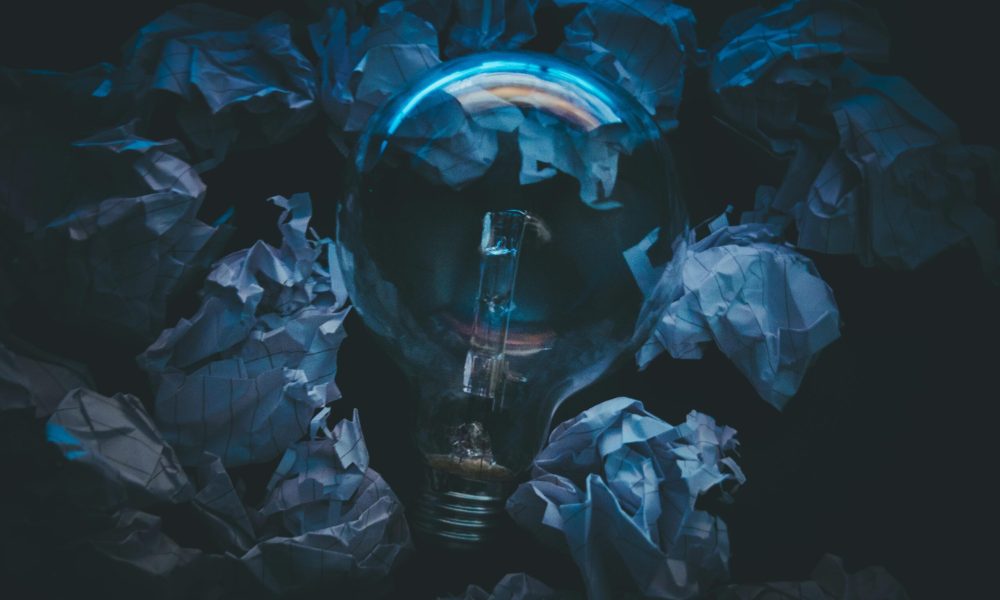 A light bulb surrounded by crumpled paper symbolizes creative ideas and innovation in a dark setting.