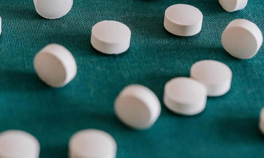Closeup of similar round white pills spilled on green tissue in random order