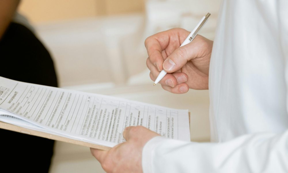 A medical professional in a white coat examines a clipboard with patient documents.