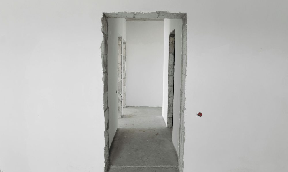 Interior view of a simple white corridor in an unfinished building, showing raw construction details.